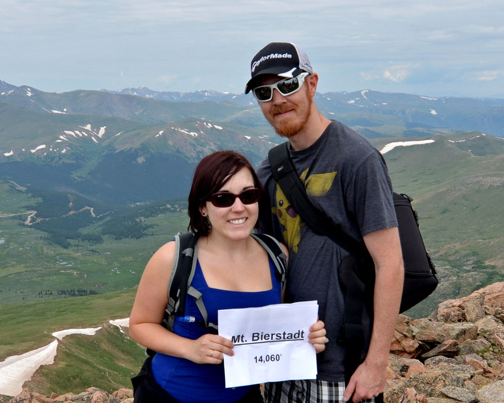 Brooke and Buddy of TrailingAway.com on the summit of Mt. Bierstadt with a sign showing the elevation.