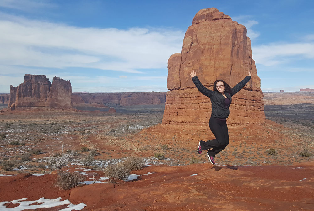 Brooke jumping in front of the red rocks along Arches Scenic Drive in Arches National Park
