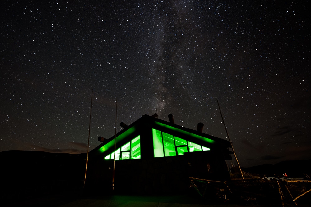 Atop Trail Ridge Road at the visitor center with the green light shining in the building and the milky way over it.