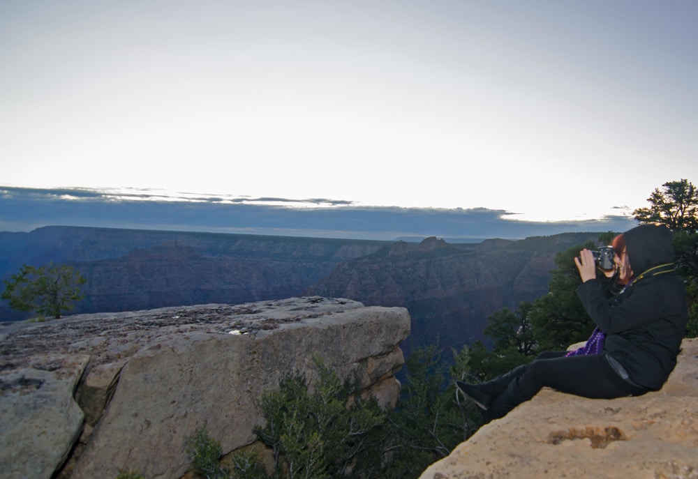 Brooke sitting on the edge of the Grand Canyon taking a photo