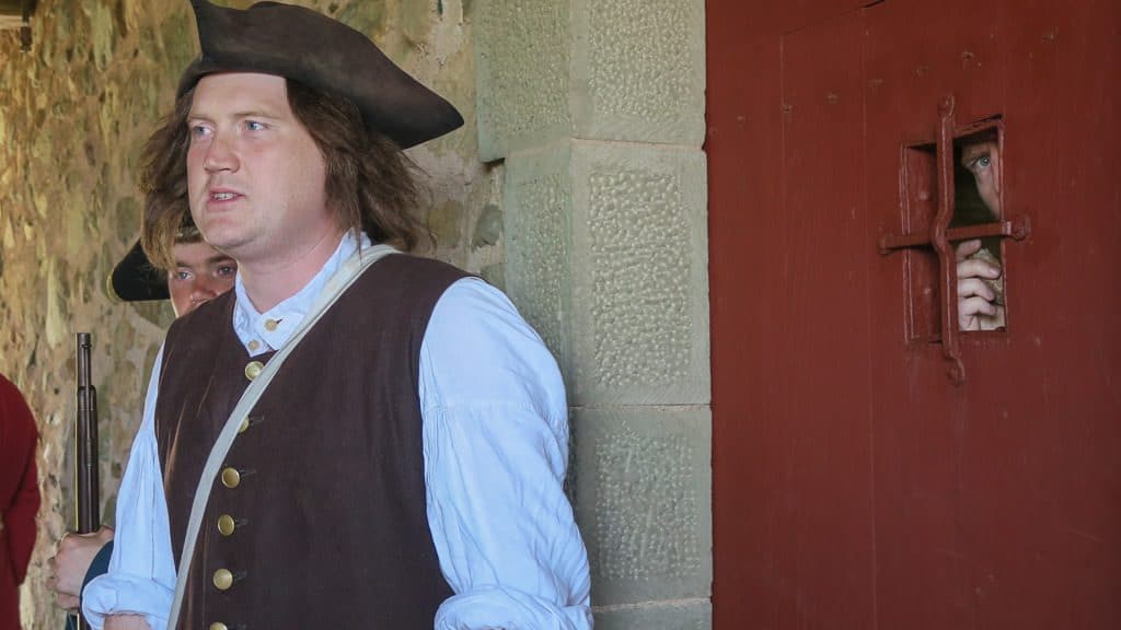 Buddy locked in the jail cell, with a guard standing outside, during his time as Prisoner of the Day at Fortress of Louisbourg