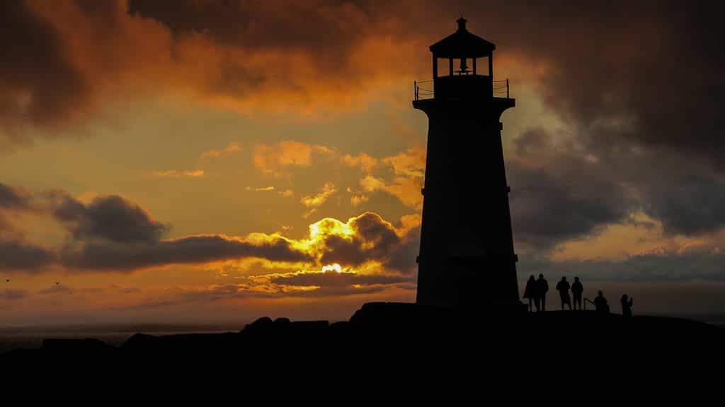 Sunset at Peggy's Cove Lighthouse in Nova Scotia with people standing next to the lighthouse