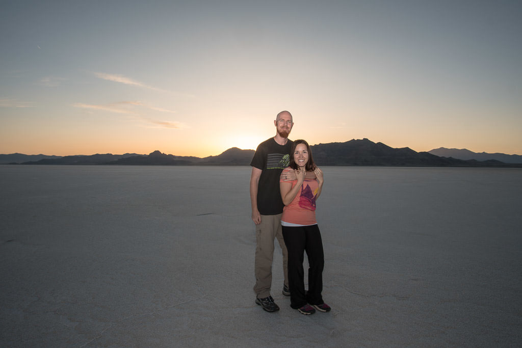 Brooke and Buddy on the bonneville salt flats as the sun sets behind the mountains behind them - best time to vsit utah salt flats is at night!