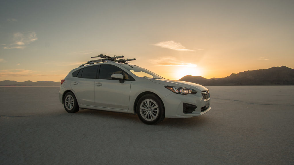 Our Subaru on the Bonneville Salt Flats with the sun setting behind the mountains in the background