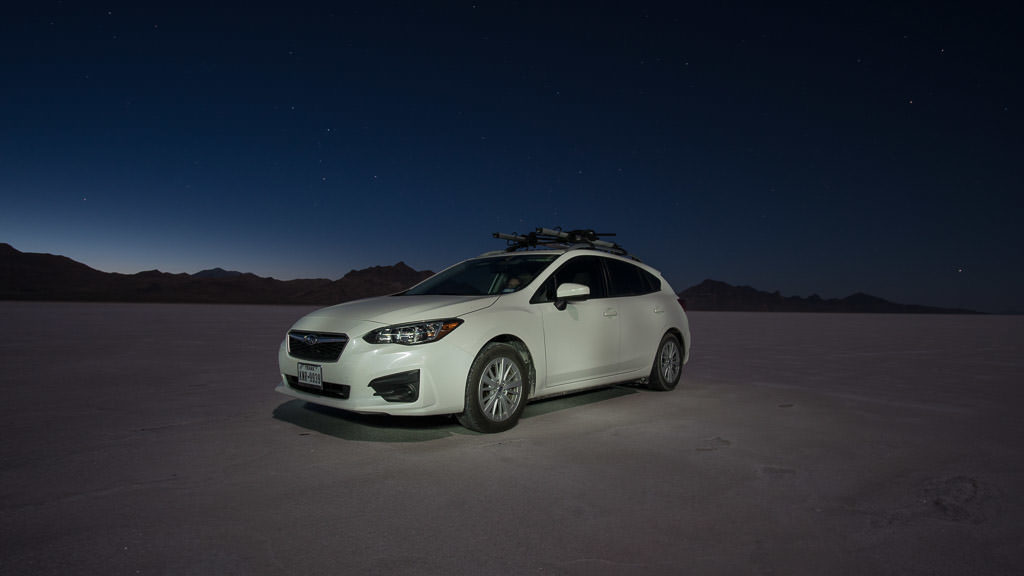 Our Subaru on the bonneville salt flats at night with stars in the sky and the silhouette of the mountains in the background