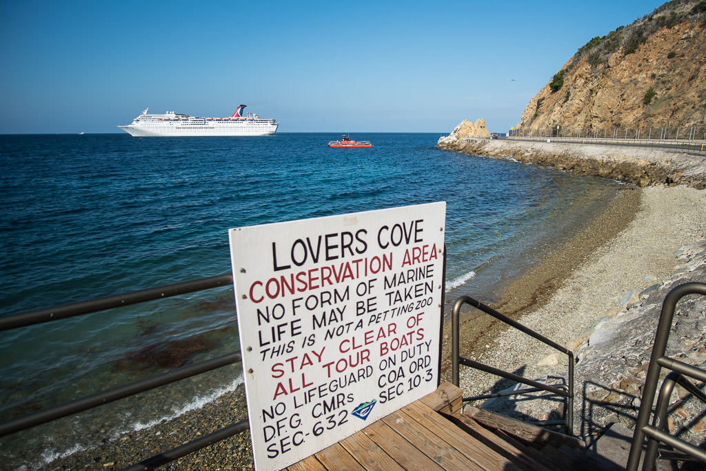 Sign for Lovers Cove conservation area in Avalon Harbor with a cruise ship and the Undersea Expedition submarine in the distance