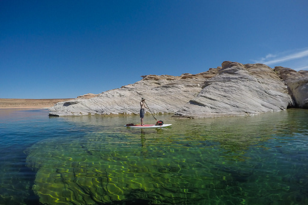 Buddy Paddleboarding on the clear water of Lake Powell next to a rock and you can see in the water 40 feet under him