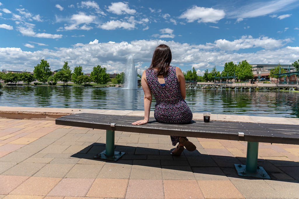 Brooke sitting on a bench enjoying some sun and drinking a coffee at a water feature outside the Westin Hotel