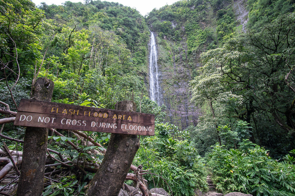 Waimoku Falls in the background behind a sign warning visitors of the dangers of Flash Floods
