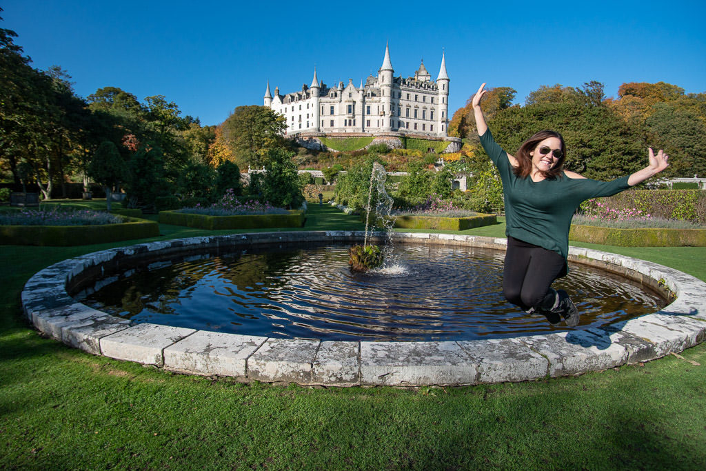 Brooke jumping in the air near one of the fountains in the garden with the huge Dunrobin Castle in the background