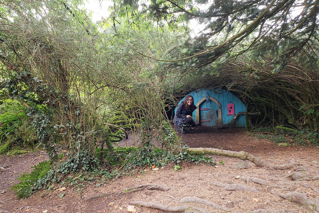 Brooke next to a tiny little house in the bushes at Giant's Lair Story Trail at Slieve Gullion Forest Park