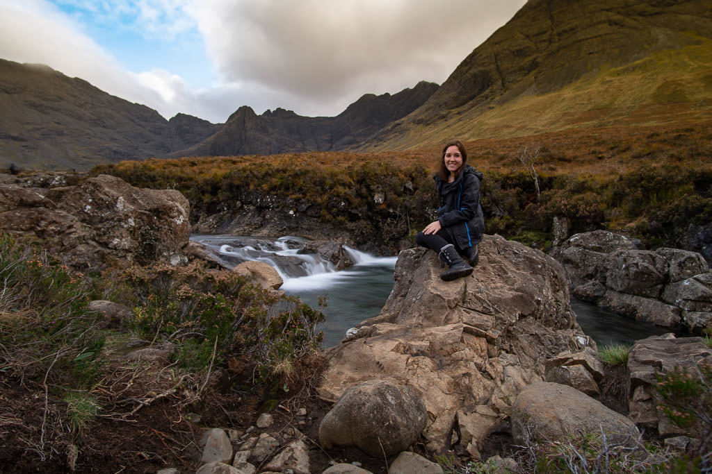 Brooke sitting on a large rock next to one of the many waterfalls at Fairy Pools in Isle of Skye