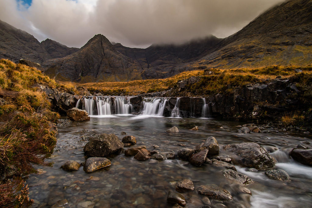 Waterfall with a dramatic mountainous scene behind it at Fairy Pools in Isle of Skye, our favorite place in Isle of Skye