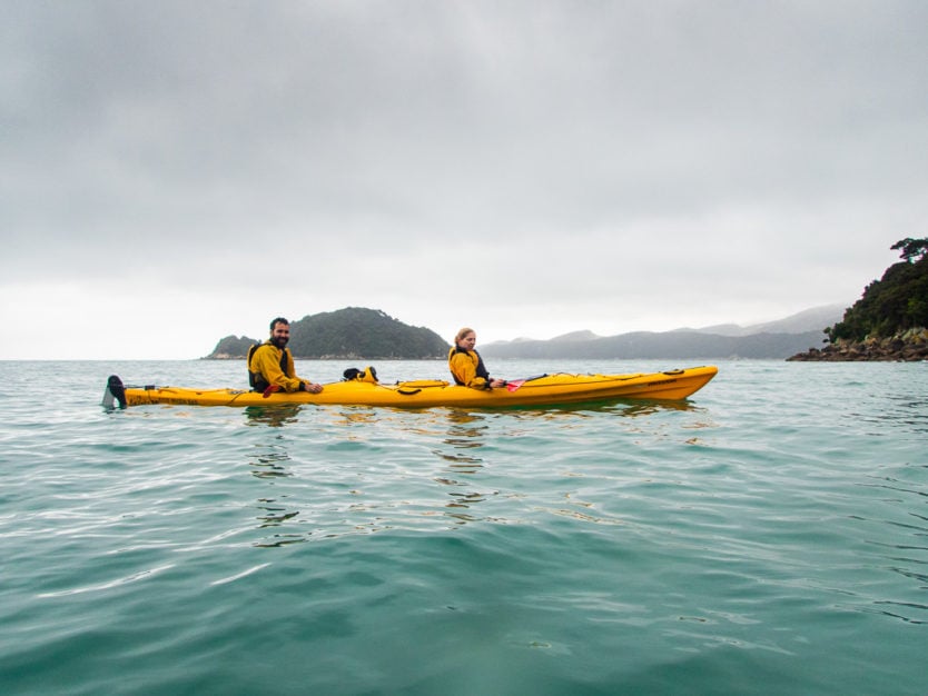 couple kayaking in abel tasman national park with tonga island in the background
