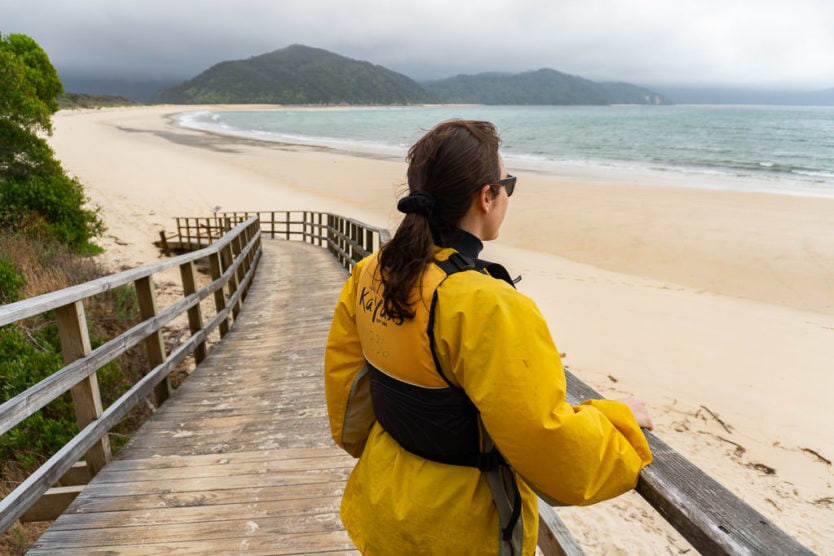 girl looking out into awaroa bay from a walkway on awaroa beach in abel tasman